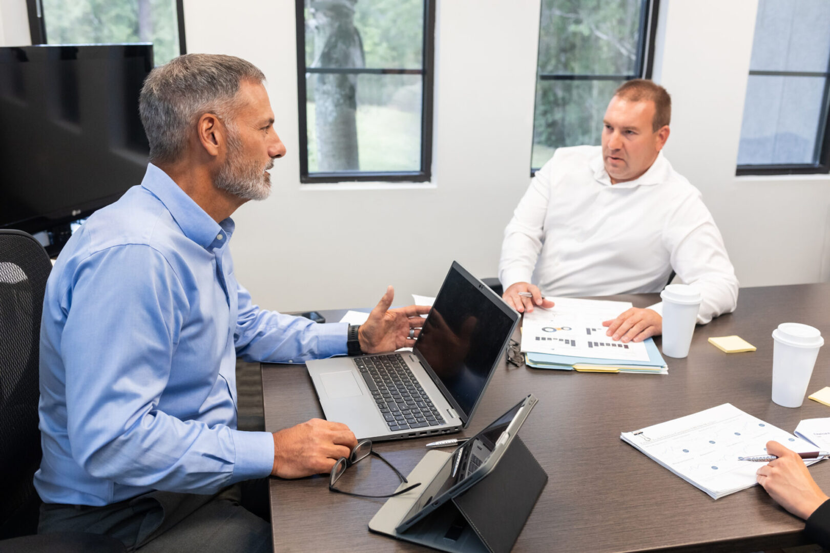 Two men sitting at a table with laptops.